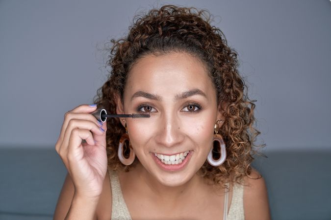 Cheerful young woman applying mascara on eyelashes