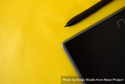 Stylus and corner of digital tablet on yellow table with space for text 5RVPZD