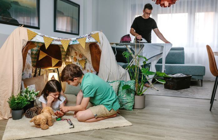 Father ironing while her children play camping at home