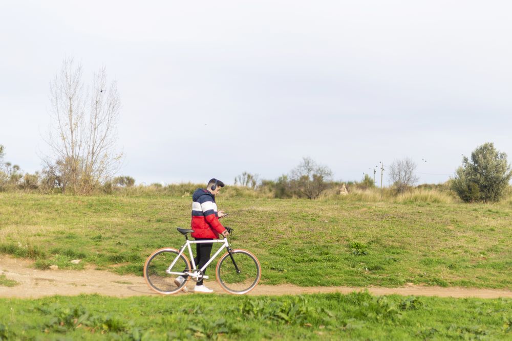 Man walking with bicycle and using a smartphone in grassy park