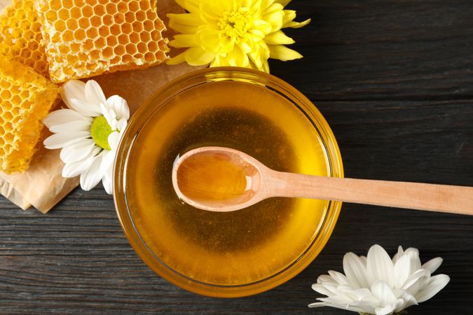 Bowl with honey, honeycombs and flowers on wooden background, top view