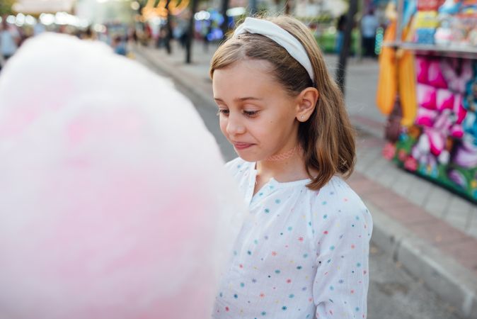 Cheerful girl eating cotton candy on street