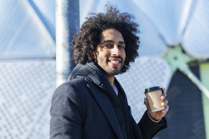 Smiling Black man in jacket with warm beverage standing outside