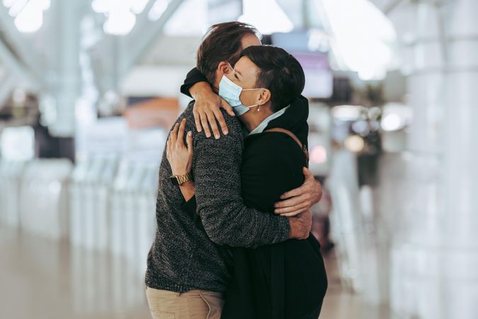 Woman receiving man at airport during pandemic