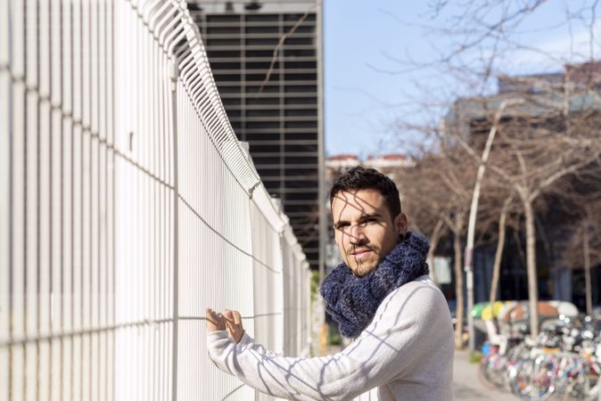 Portrait of casual male grasping metallic fence while looking at camera