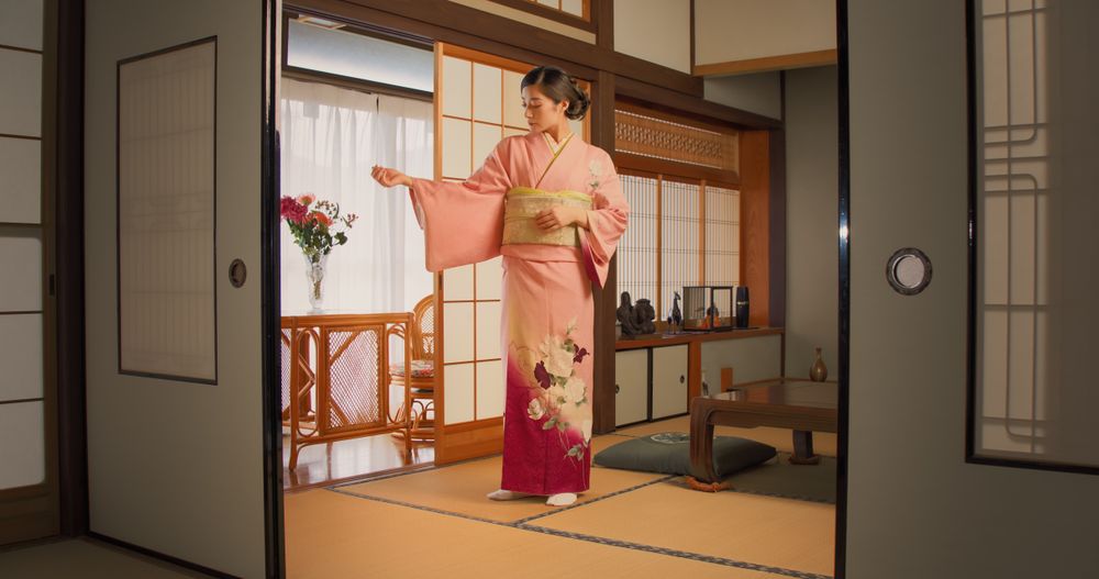 Female Wearing a Traditional Dress in Japan in a Pink Kimono with Flowers is Posing for Camera at Home.