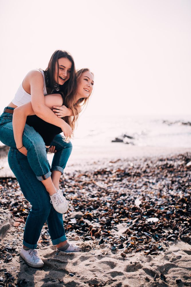 Piggyback happy female friends having fun on the beach