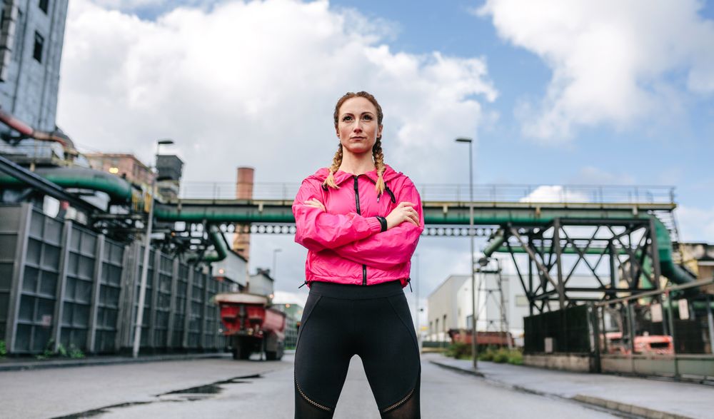 Sportswoman with crossed arms posing in front of a factory
