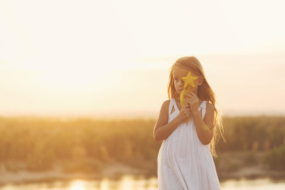 Blonde female child in summer dress standing in front of lake with star wand