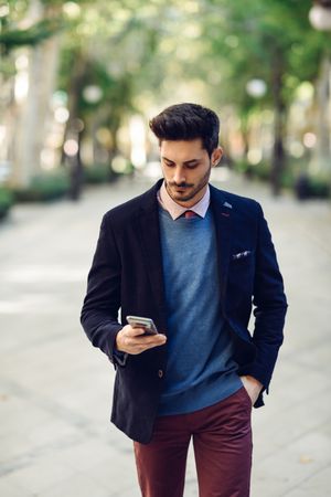 Attractive man in the street wearing elegant suit looking down at smartphone in his hand, vertical