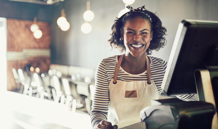 Smiling woman in apron standing at modern til