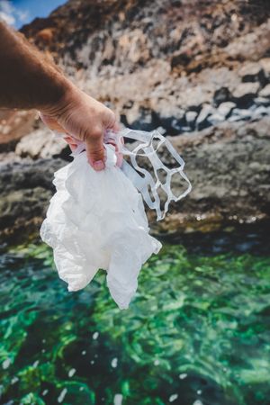 Crop man pulling plastic bag out of water