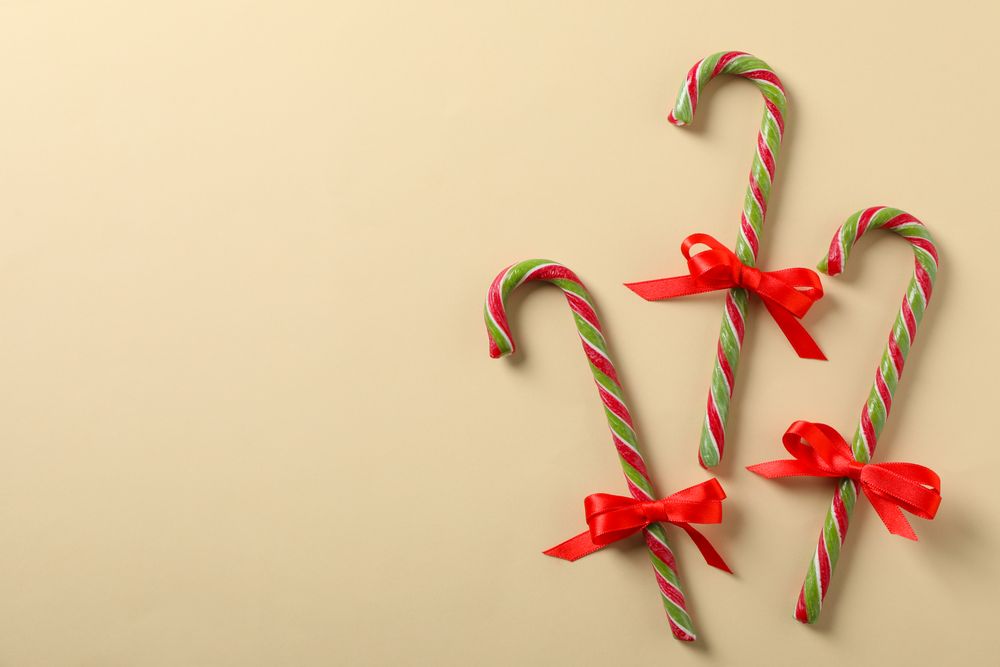 Sweet candy canes with bow on color background, space for text