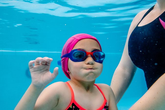 Cheerful girl underwater swimming in pool with mother