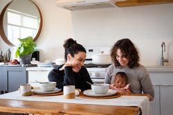 Two mothers eating soup with newborn baby at their dining table at home