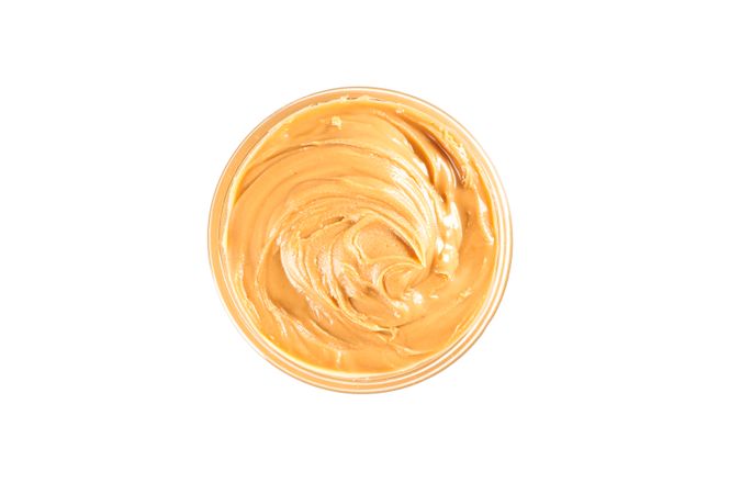 Creamy peanut butter in glass bowl isolated on light background, top view. A traditional product of American cuisine