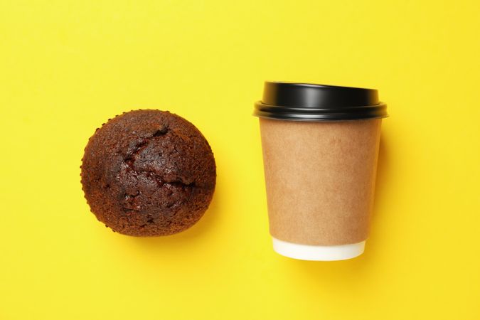 Paper cup and chocolate muffin on yellow background, space for text