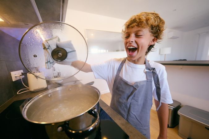 Excited boy with lid against boiling water in pot
