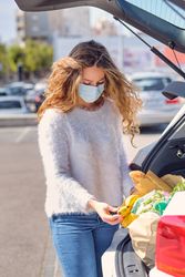 Young woman checking grocery bags in car trunk