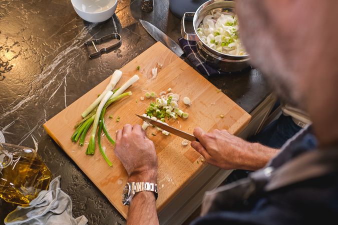Unrecognizable man cutting green onion