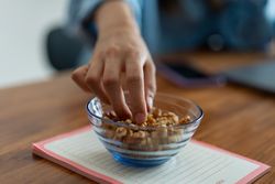 Hand picking walnuts from a glass bowl on a notebook - energy and focus during remote work