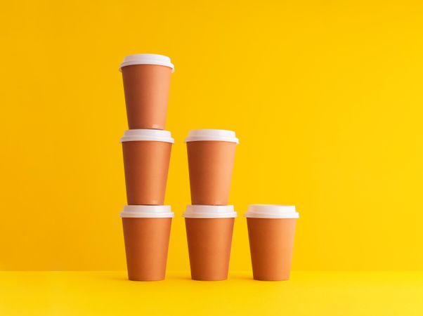 Declining stack of disposable coffee cups on yellow background