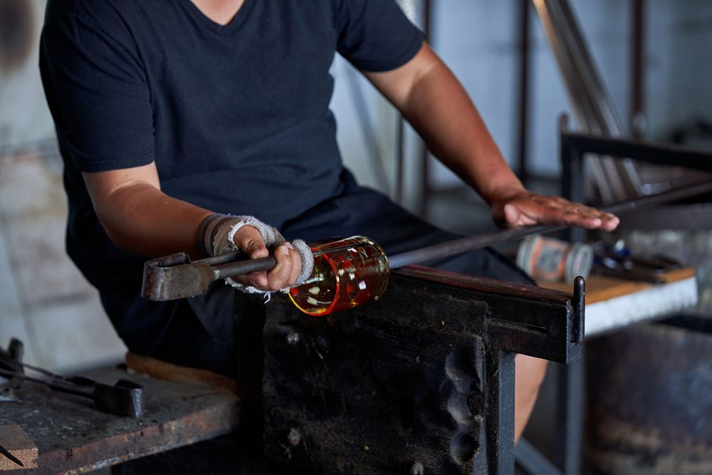 Glassblower shaping glass on rod in industry