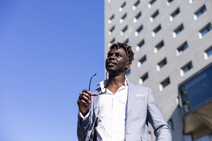 Looking up at Black man in elegant suit standing outside of building on a sunny day