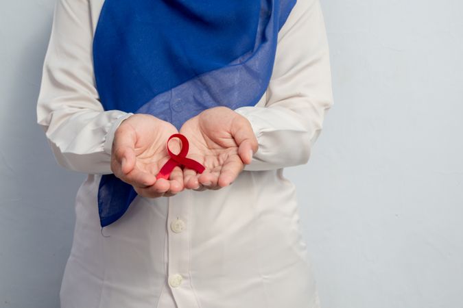 Happy Muslim Female Asian doctor or nurse holding Red ribbons, HIV awareness concept, world AIDS day, world cancer day with copy space