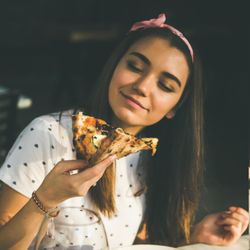 Young woman eating pizza outside in the sun, square crop