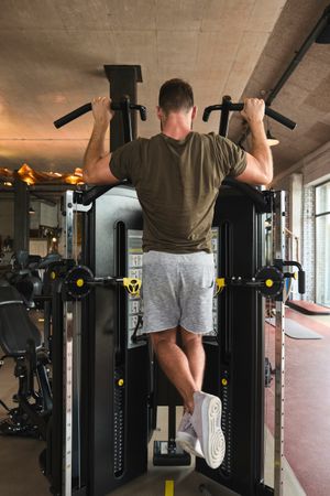Muscular guy doing pull ups on exercise machine