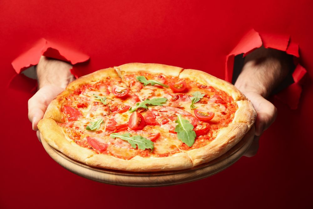 Hands hold tasty pizza on red background