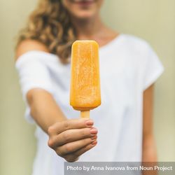 Woman in t-shirt holding orange popsicle, square crop 49NRQb