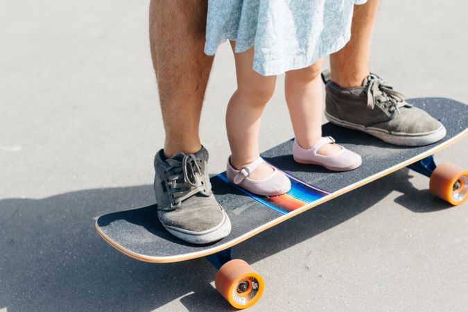 Crop father with infant daughter on skateboard