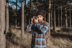 Confident photographer taking picture with camera in sunny forest
