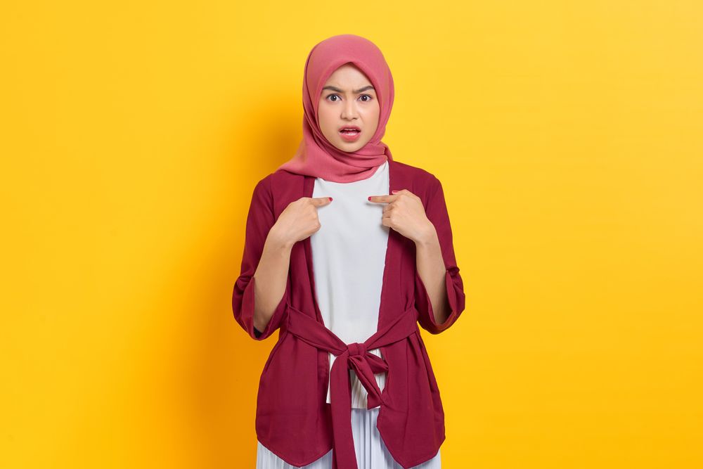 Incredulous woman in red headscarf pointing at herself questioningly