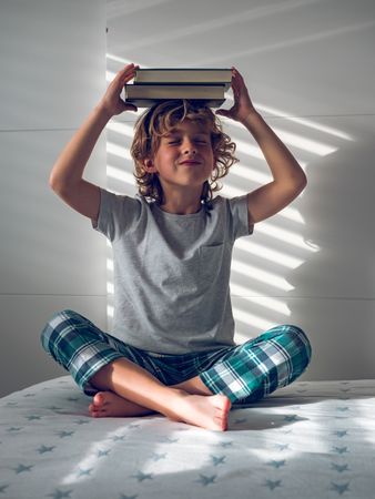 Little boy putting pile of books on head