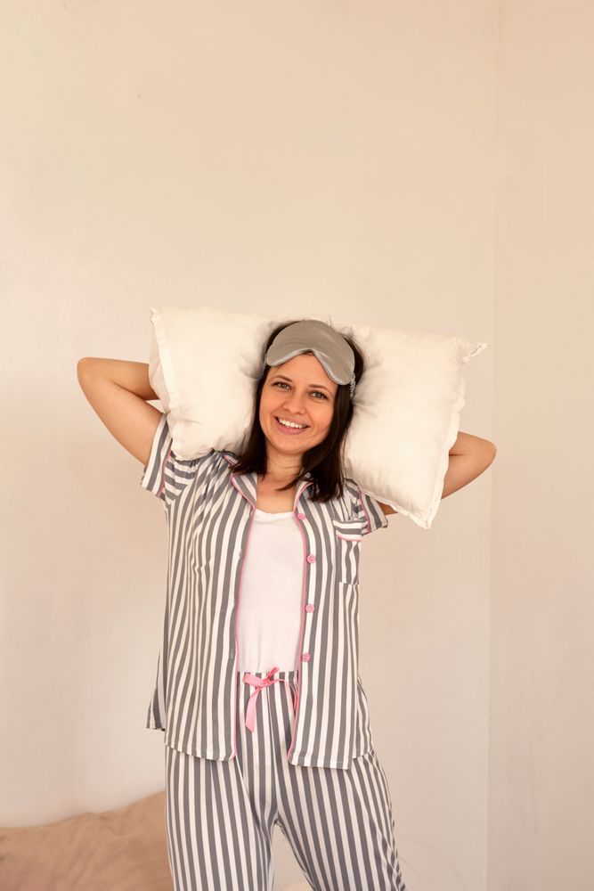 Woman smiling, holding pillows while standing in bed.