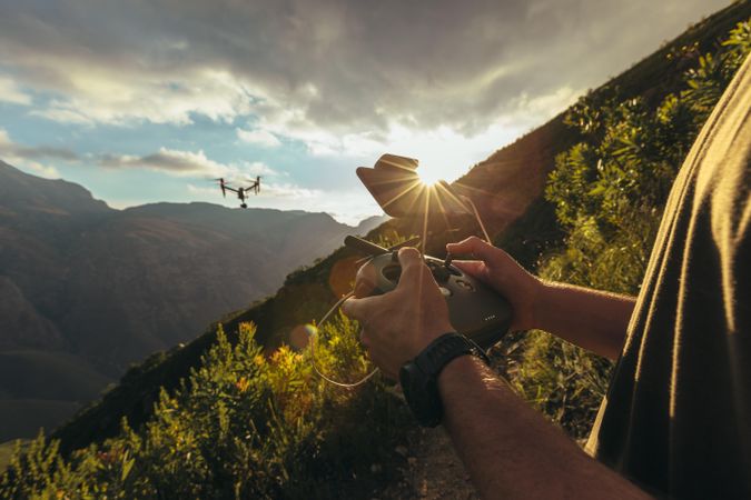Close up of man hands controlling a drone flying over mountains with remote control