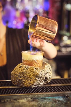 Crop woman pouring ingredient into cocktail glass in nightclub