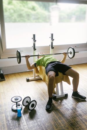 Man in green t-shirt lifting heavy bar on bench working out arms and chest