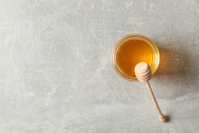 Glass jar with honey and dipper on grey background, copy space