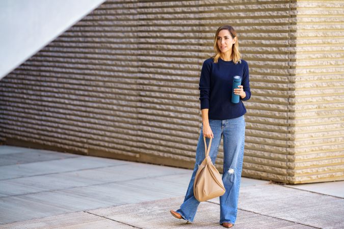 Stylish female standing on street with thermos