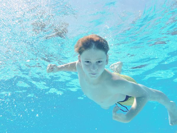 Funny boy swimming underwater looking at camera