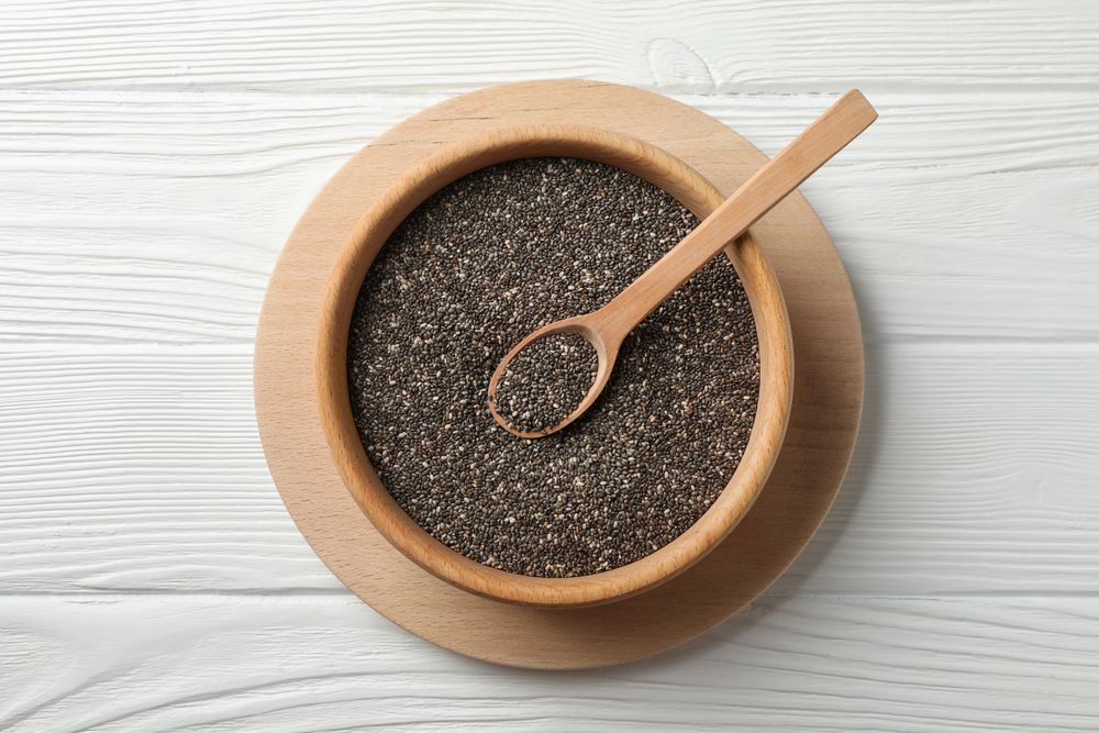 Wooden bowl with chia and spoon on wooden background, top view