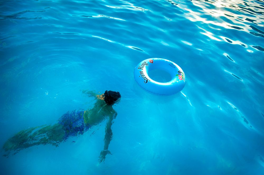 Person swimming underwater near inflatable ring in swimming pool