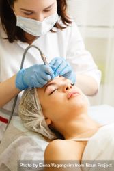 Woman having beauty treatment with instrument on her forehead, vertical bxxEZb