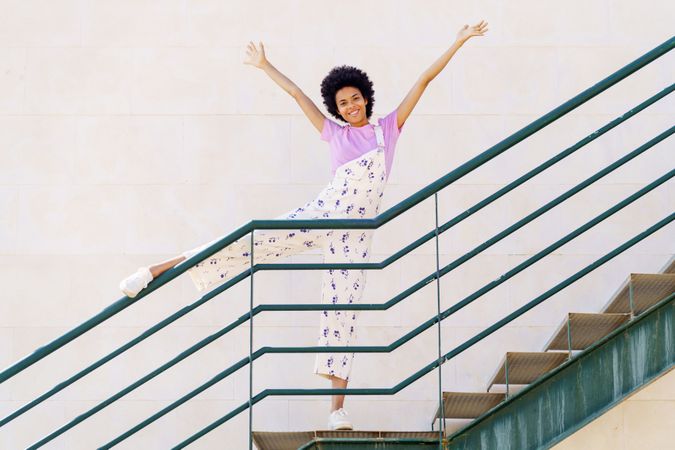 Happy woman on stairs with leg up on green handrail and arms up