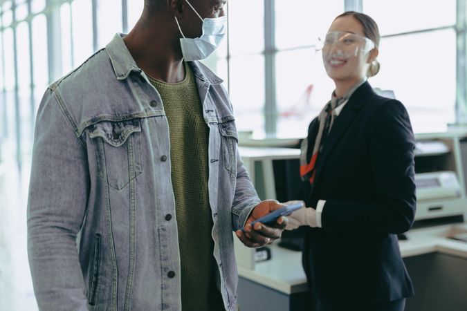 Male passenger in face mask at check-in counter with airport staff