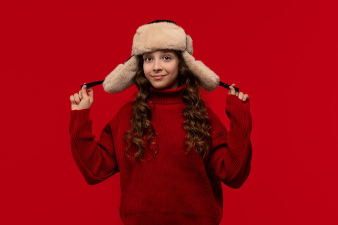Smiling girl in fur hat holds ear flaps of hat